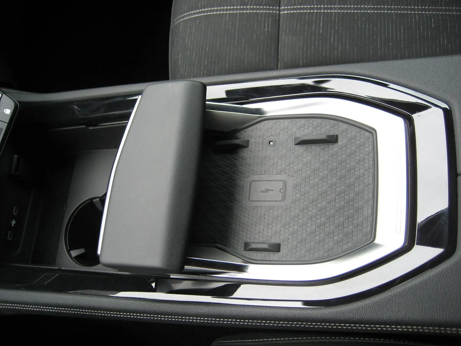 Gros plan intérieur sur la console centrale noire du Renault Austral gris, mettant en valeur le repose-bras et le chargeur sans fil.