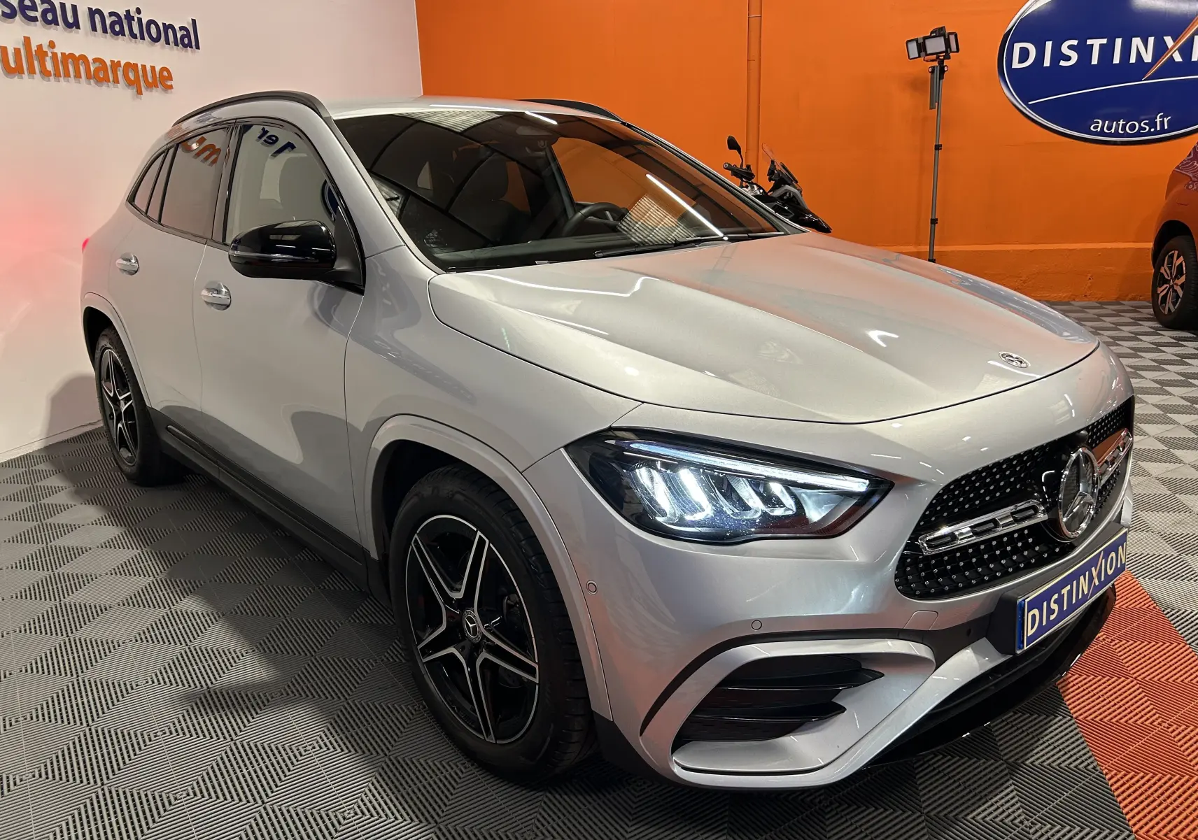 Mercedes GLA 200 D AMG Line argent High-tech en 3/4 avant droit, avec jantes AMG noires et phares LED allumés.