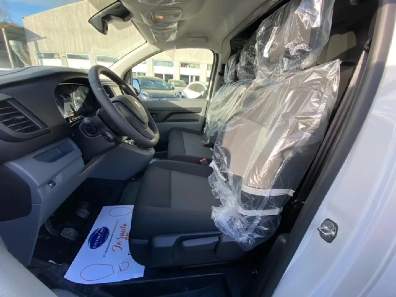 Vue intérieure côté conducteur du Peugeot Expert Fourgon blanc banquise 2023, sièges avant protégés par film plastique.