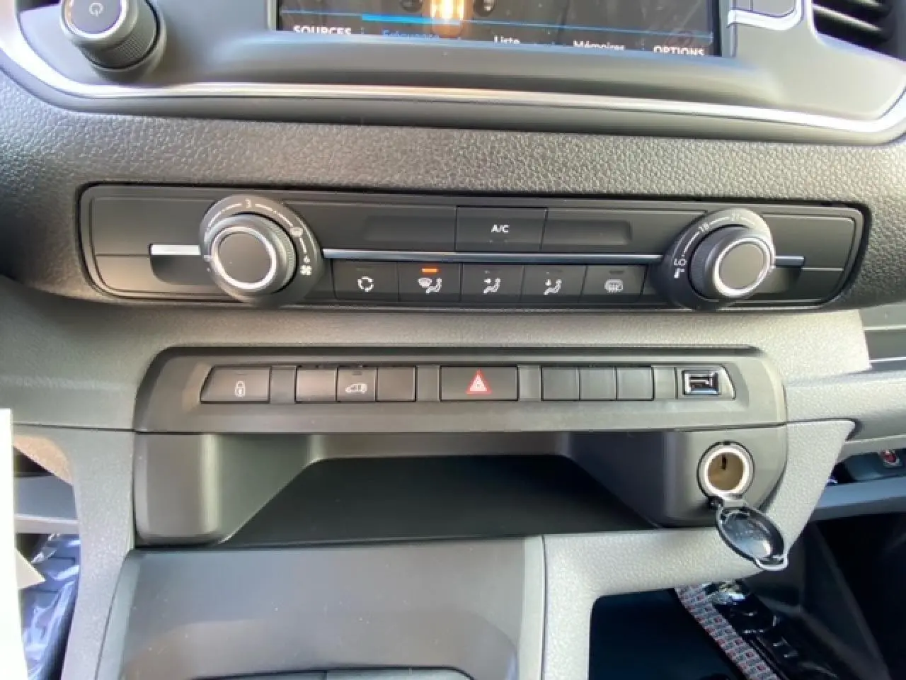 Gros plan sur la console centrale du Peugeot Expert Fourgon blanc, montrant les commandes de climatisation et les boutons de sécurité.