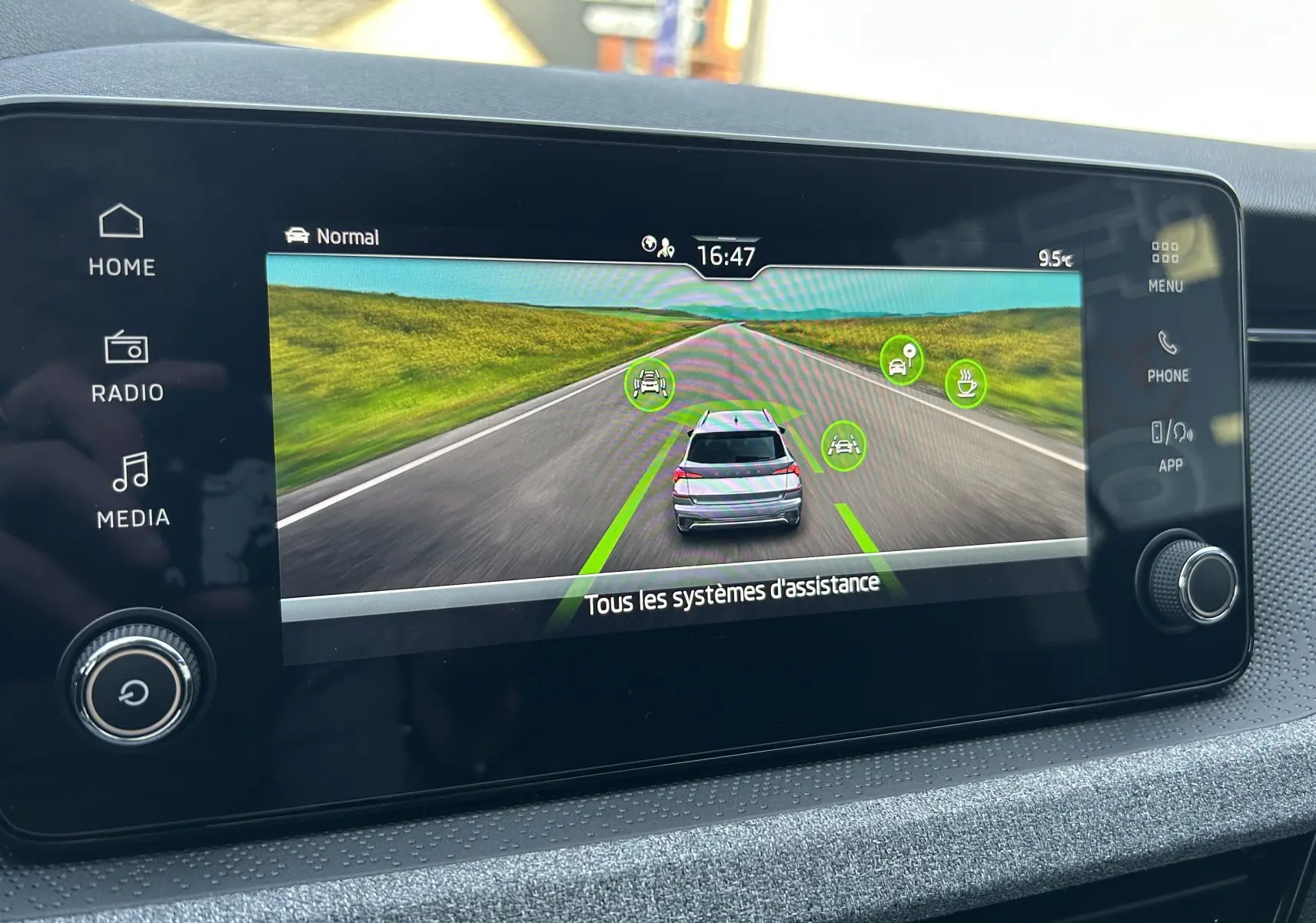 Écran tactile intérieur montrant l'assistance à la conduite avec une Skoda Kamiq gris argent sur route virtuelle.