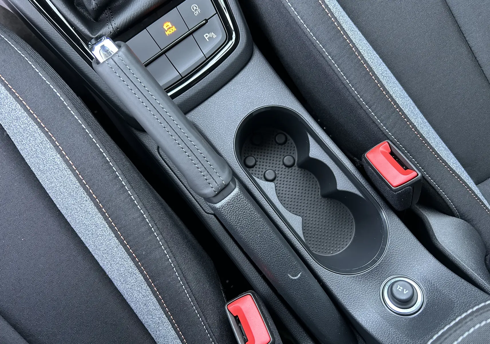 Détail intérieur de la console centrale grise avec frein à main cuir, porte-gobelets et boutons de commande sur Skoda Kamiq 2025.