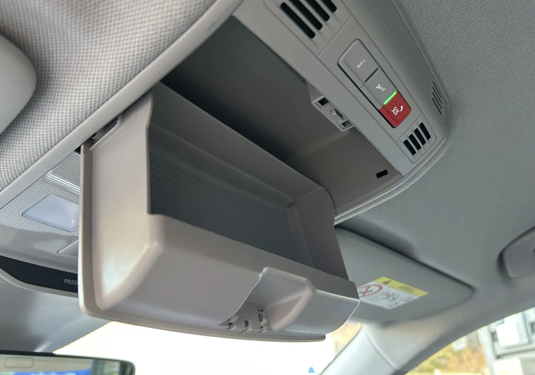 Vue intérieure en plongée du rangement lunettes ouvert gris clair au plafond d'un Skoda Kamiq 2025, avec commandes d'urgence visibles.