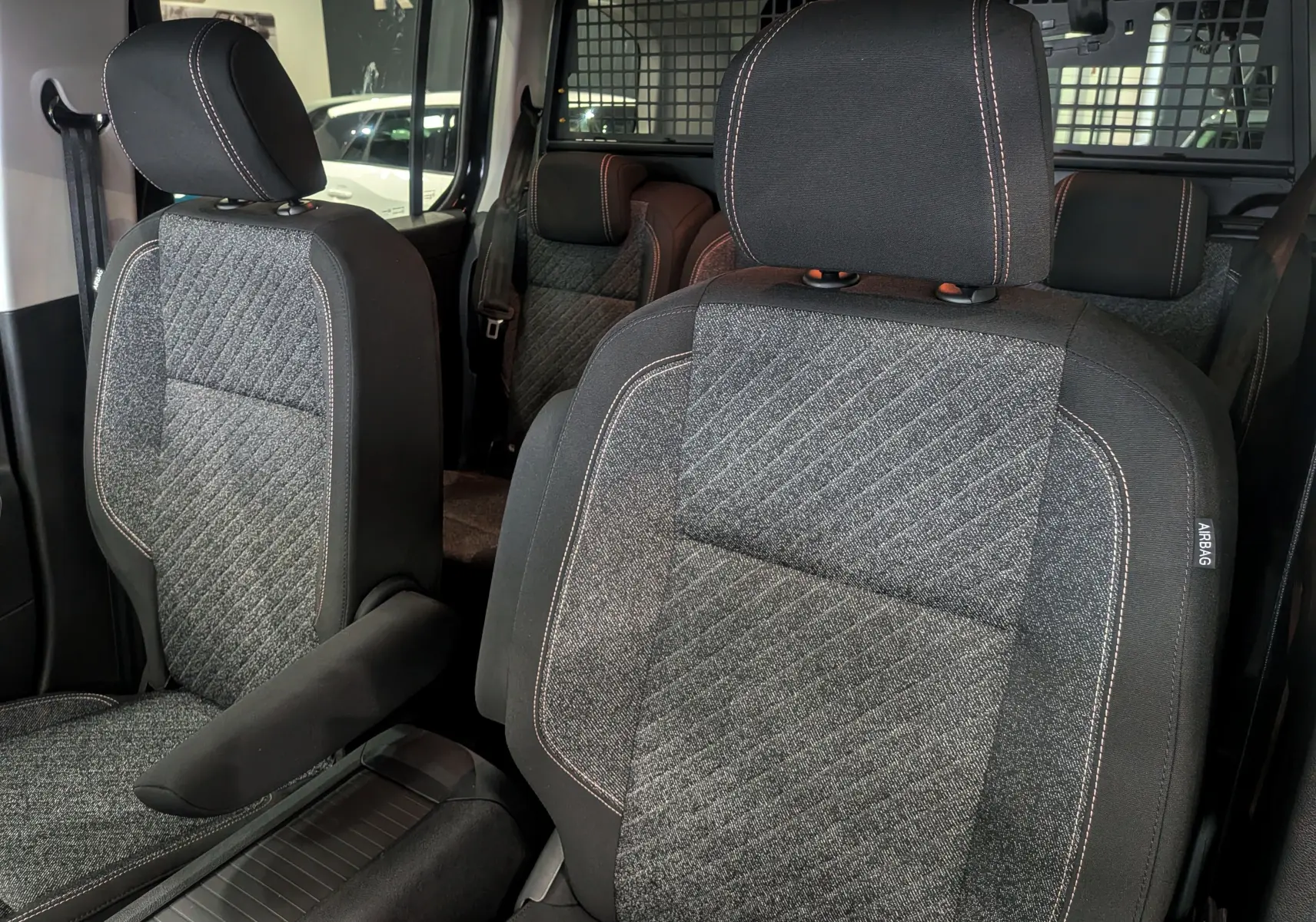 Gros plan sur les sièges avant en tissu gris et noir du Peugeot Rifter 2025, version Allure, avec surpiqûres contrastantes.