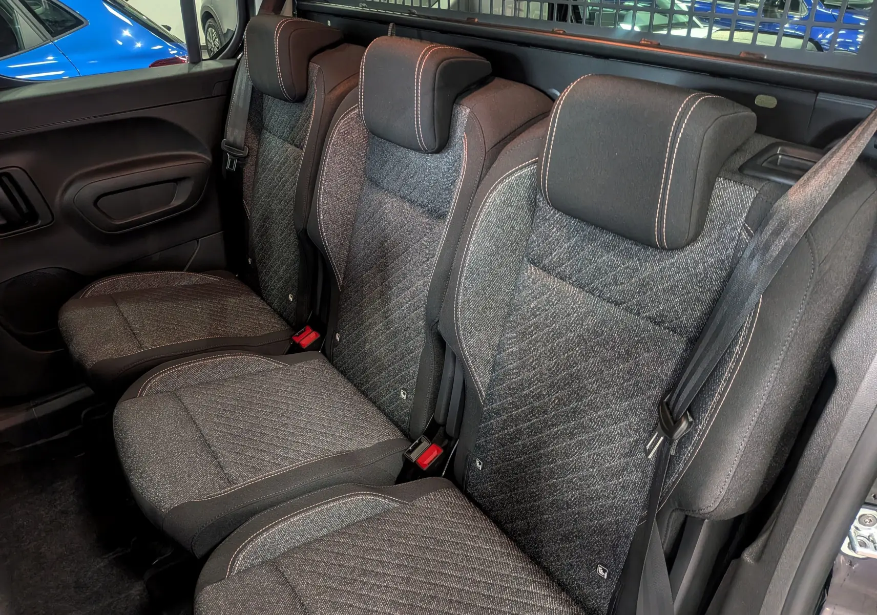 Vue intérieure côté droit des sièges arrière en tissu gris du Peugeot Rifter noir, avec appuie-têtes et ceintures de sécurité visibles.