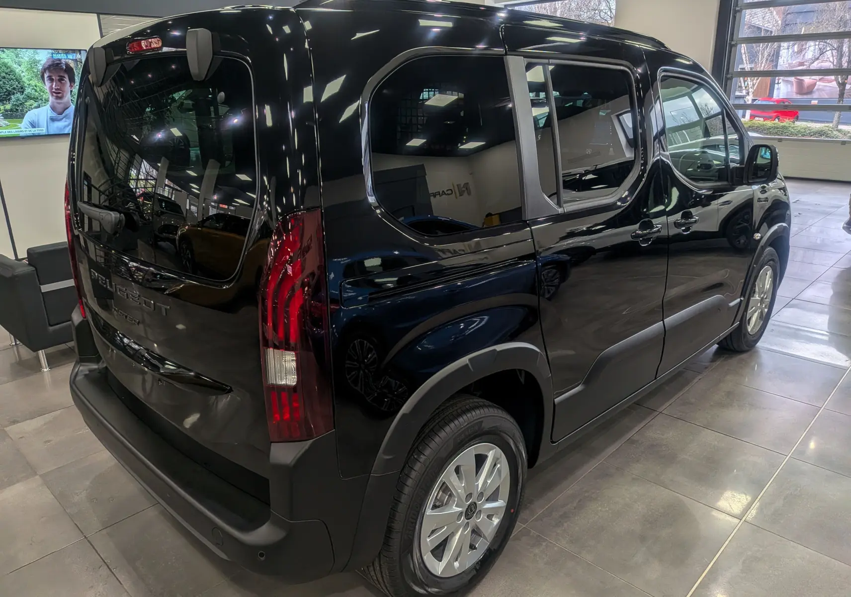 Peugeot Rifter noir vue 3/4 arrière droit en intérieur, avec feux arrière verticaux et jantes alliage 16 pouces.