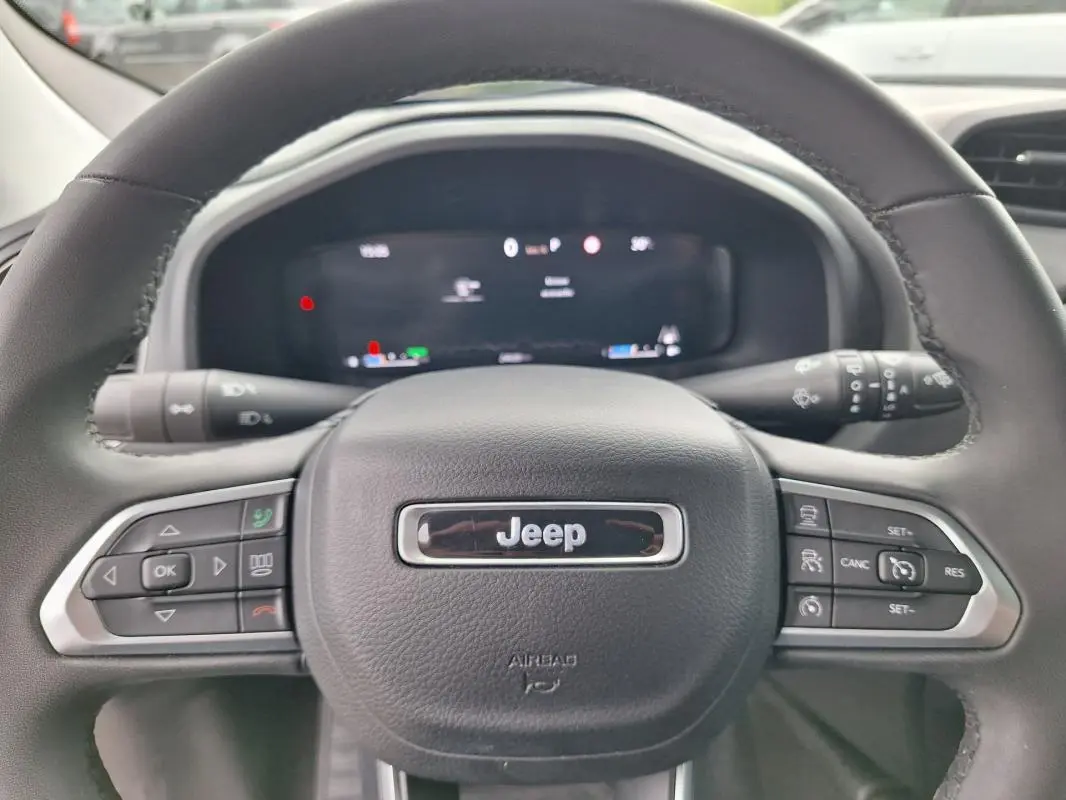 Vue rapprochée du volant noir de la Jeep Renegade 2024 avec commandes intégrées et écran numérique flou en arrière-plan.
