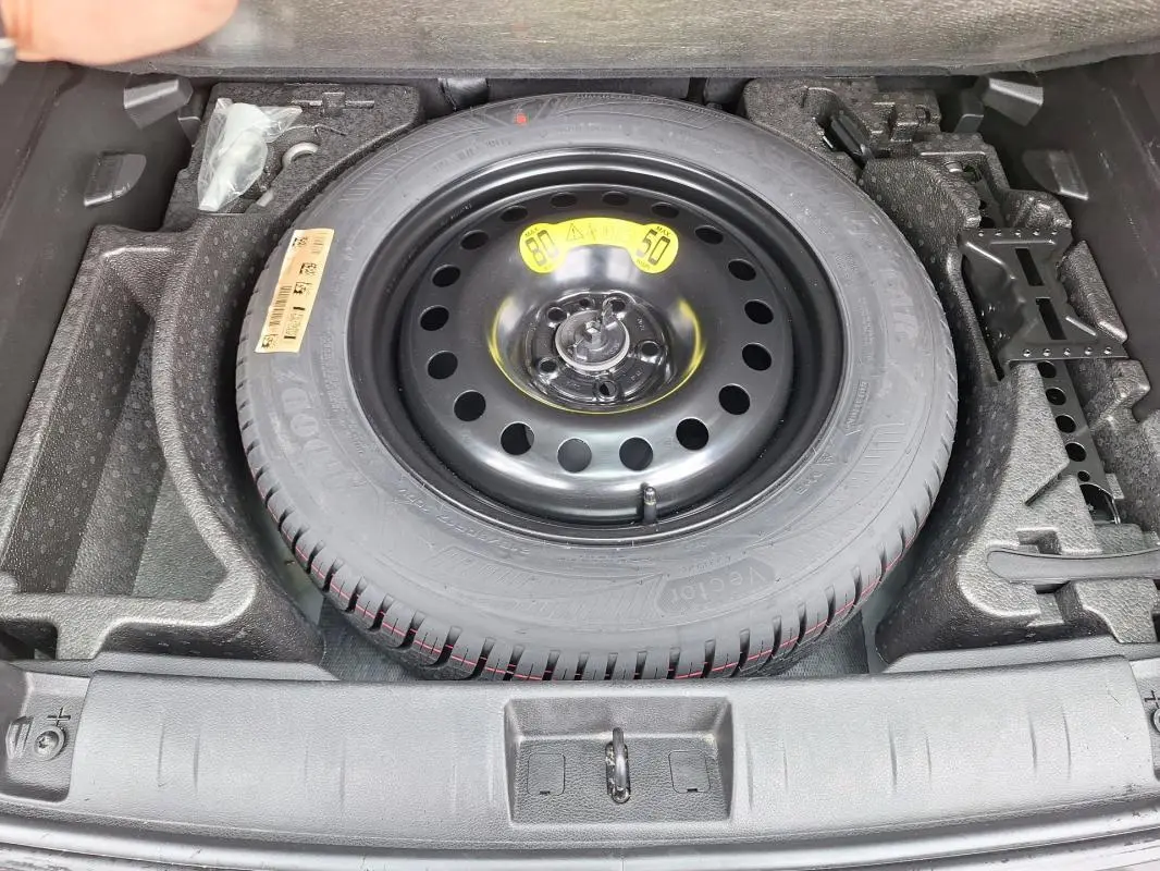 Vue plongeante sur la roue de secours noire et ses outils de bord dans le coffre du Jeep Renegade 2024.