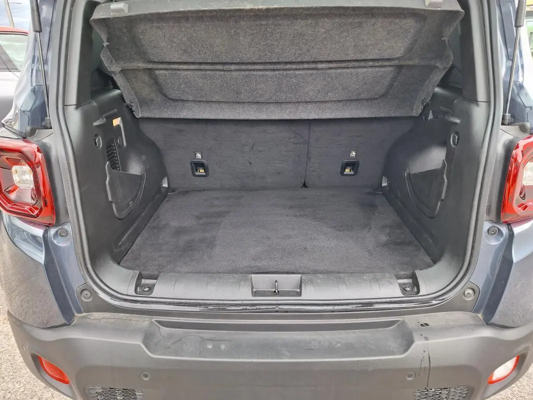 Coffre ouvert vu de l'arrière d'un Jeep Renegade bleu 2024, montrant l'espace de chargement vide et la moquette noire.