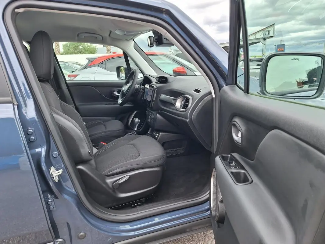 Vue intérieure côté conducteur d'un Jeep Renegade bleu 2024, montrant sièges noirs et tableau de bord moderne.