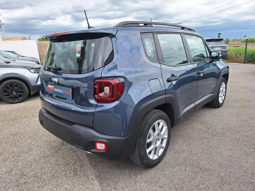 Jeep Renegade bleu en vue 3/4 arrière droit, avec barres de toit et jantes alliage 17 pouces visibles.