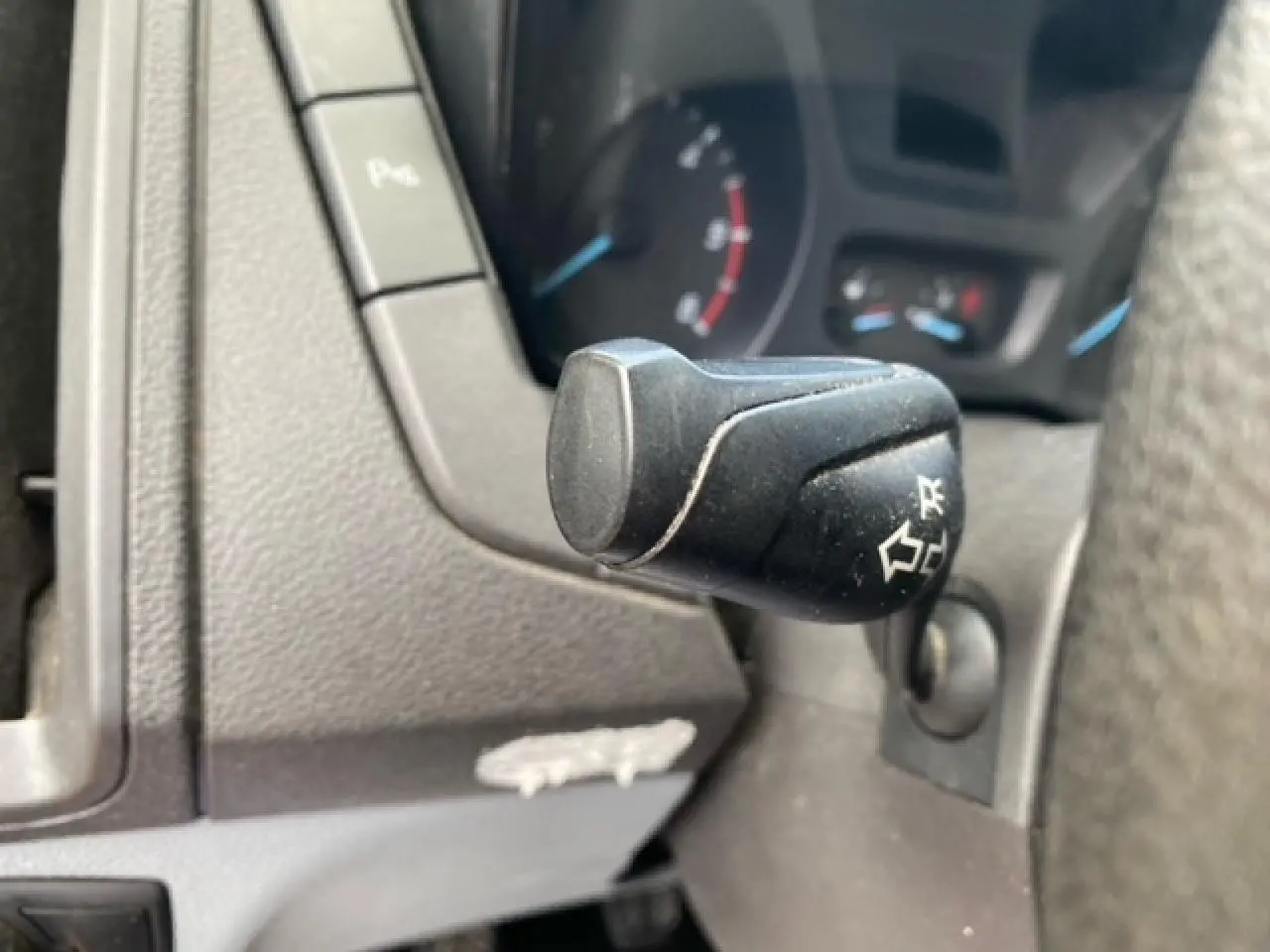 Gros plan sur la commande de clignotant noire du Ford Transit Fourgon L3H2 2015, tableau de bord gris visible en arrière-plan.