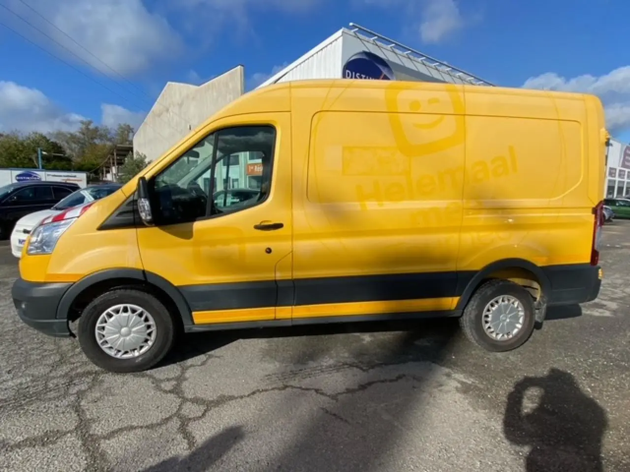 Fourgon Ford Transit L3H2 orange vu de profil côté gauche sur un parking ensoleillé.