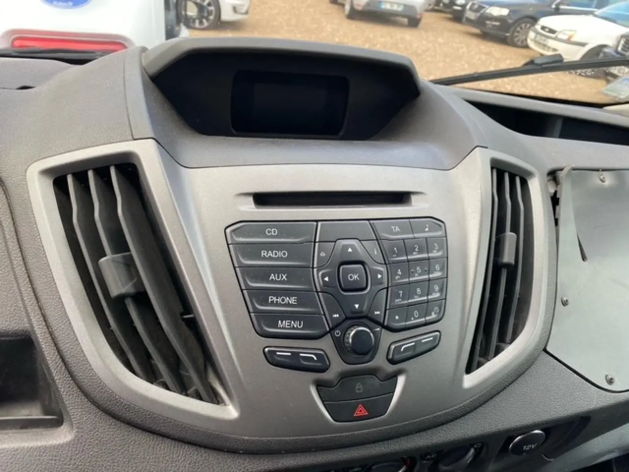Tableau de bord central du Ford Transit Fourgon L3H2 2015 avec commandes audio et ventilation visibles, intérieur gris.