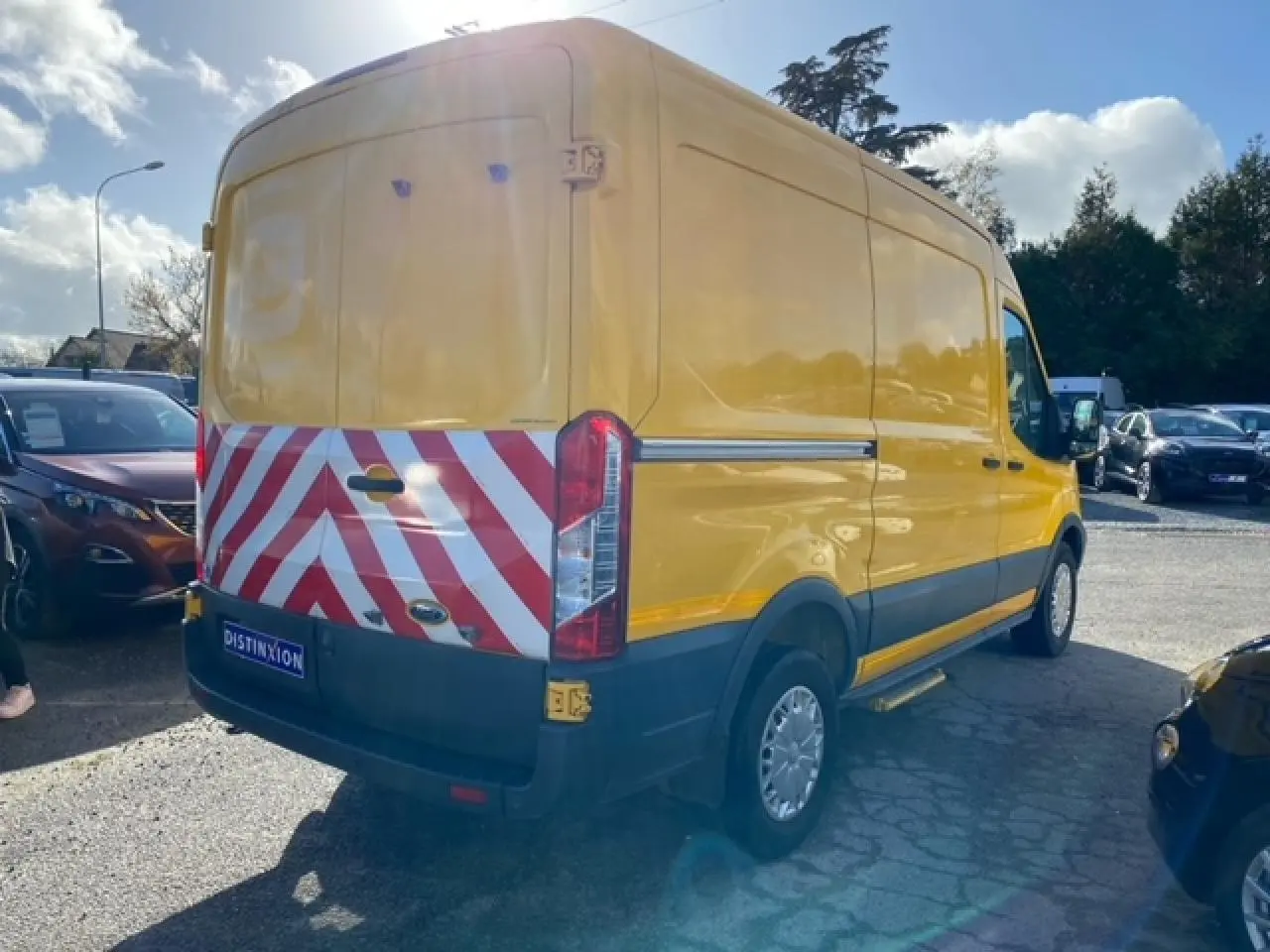 Ford Transit Fourgon orange vu en 3/4 arrière droit avec marquage rouge et blanc sur portes arrière tôlées.