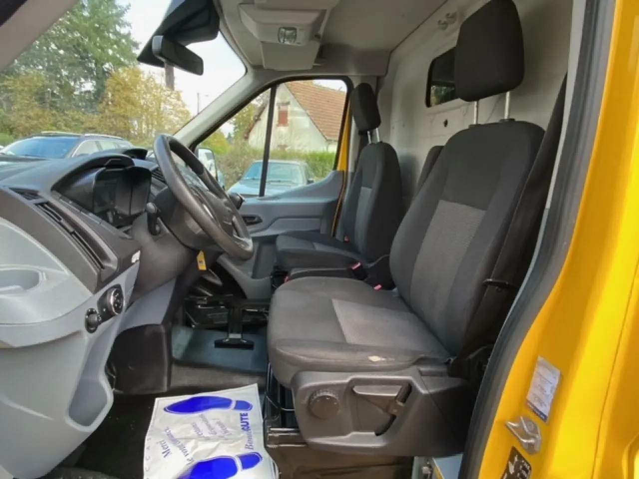 Intérieur du Ford Transit Fourgon orange 2015, vue côté conducteur montrant les sièges avant et le tableau de bord.