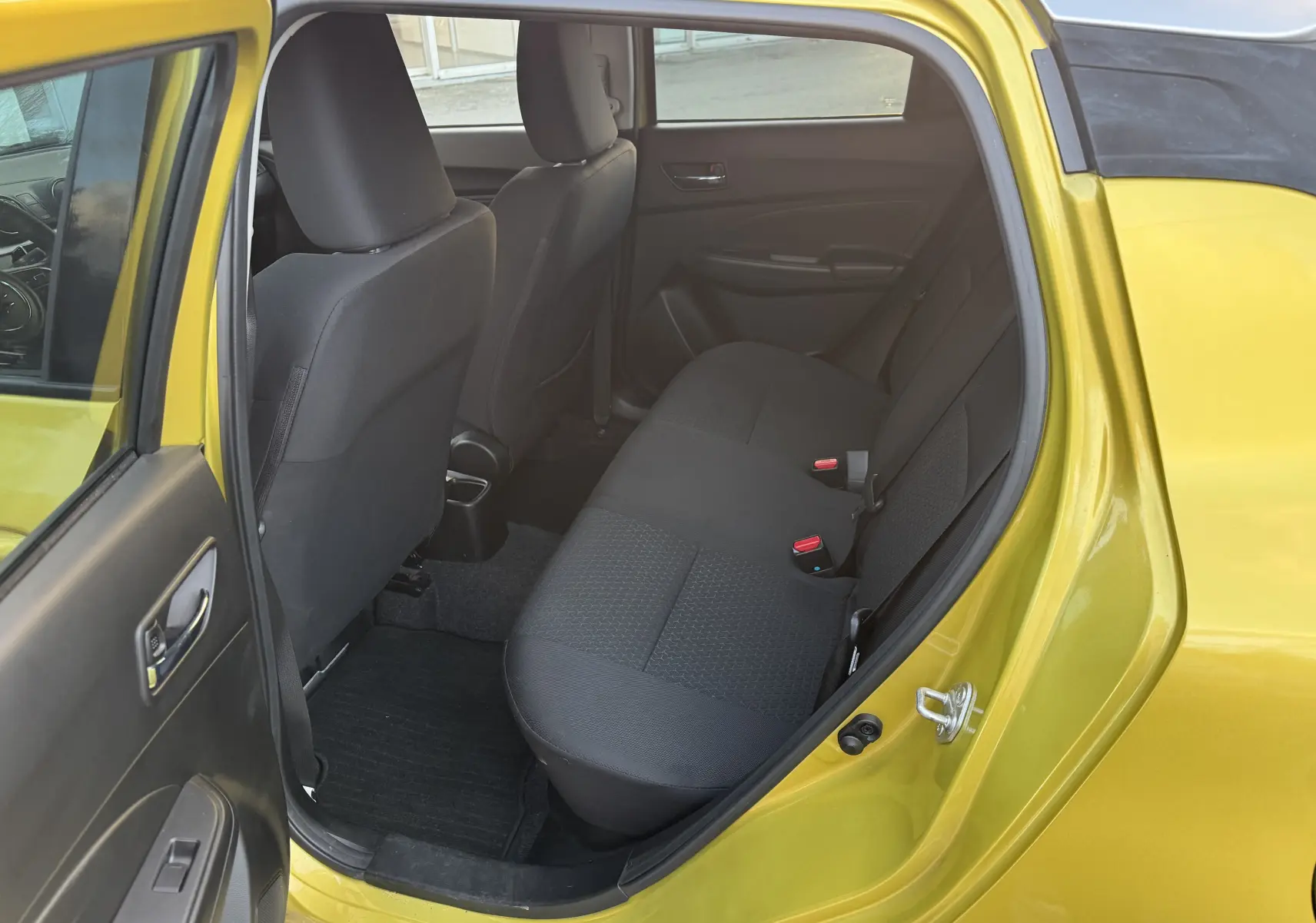 Vue intérieure arrière gauche d'une Suzuki Swift 1.2 Pack Auto 2023 jaune/gris, montrant les sièges arrière noirs et la porte ouverte.