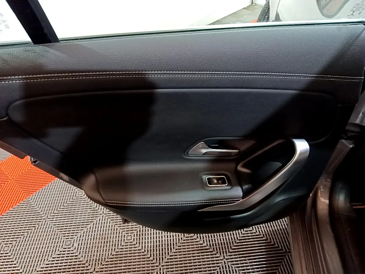 Vue intérieure côté gauche de la porte noire de la Mercedes CLA 180 d Business Line avec poignée argentée et bouton de vitre électrique.