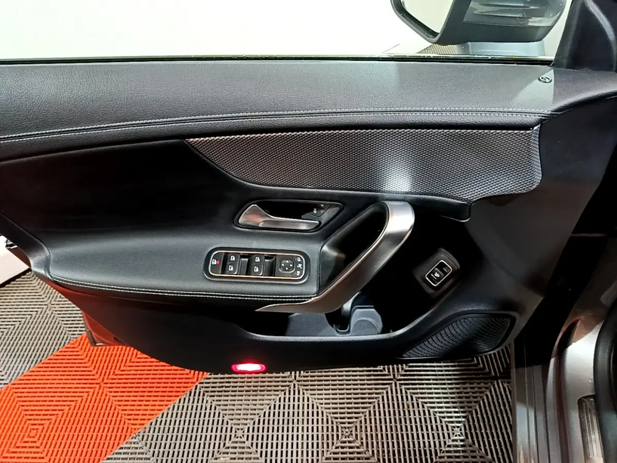 Vue rapprochée de la porte intérieure côté conducteur noire avec commandes électriques et poignée argentée d’une Mercedes CLA 180 d 2021.
