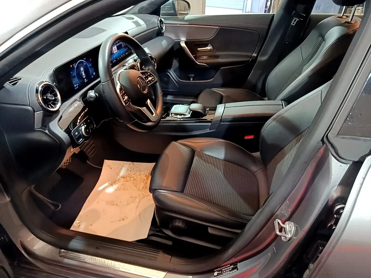 Vue intérieure côté conducteur de la Mercedes CLA 180 d Business Line 2021 gris clair, avec tableau de bord numérique et sièges en cuir noir.