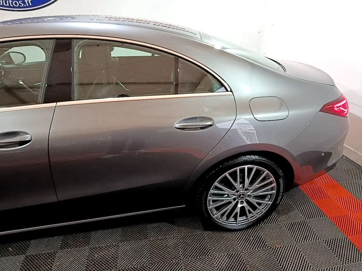 Vue côté droit arrière d'une Mercedes CLA 180 d Business Line gris clair avec jante alliage et feux arrière LED allumés.