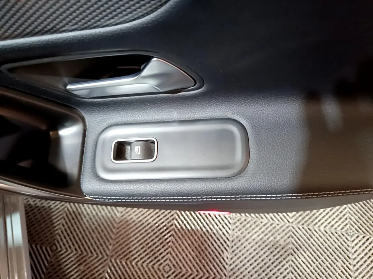 Gros plan sur la commande de lève-vitre et poignée intérieure en cuir noir sur la porte côté conducteur d'une Mercedes CLA 180 d gris clair.