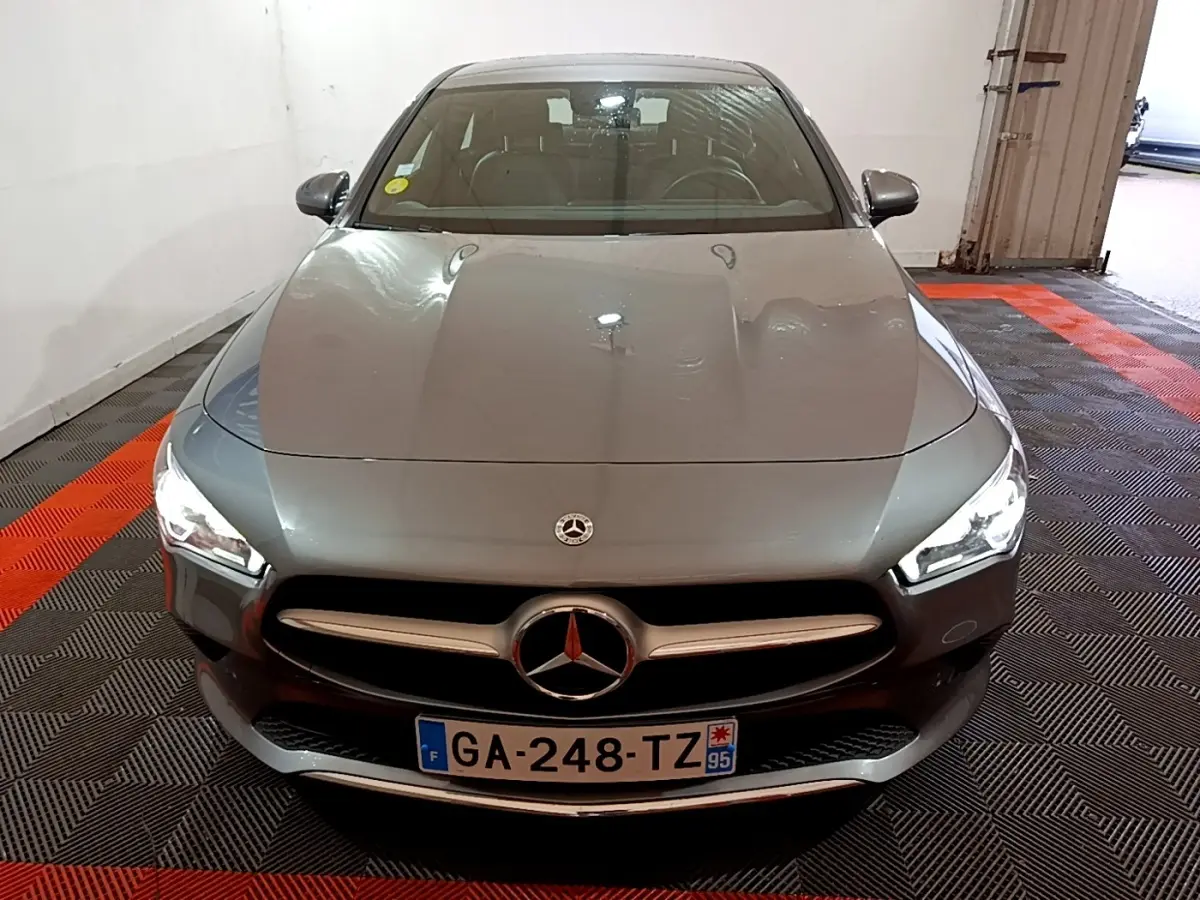 Vue avant d'une Mercedes CLA 180 d Business Line gris clair, avec phares LED allumés dans un garage.