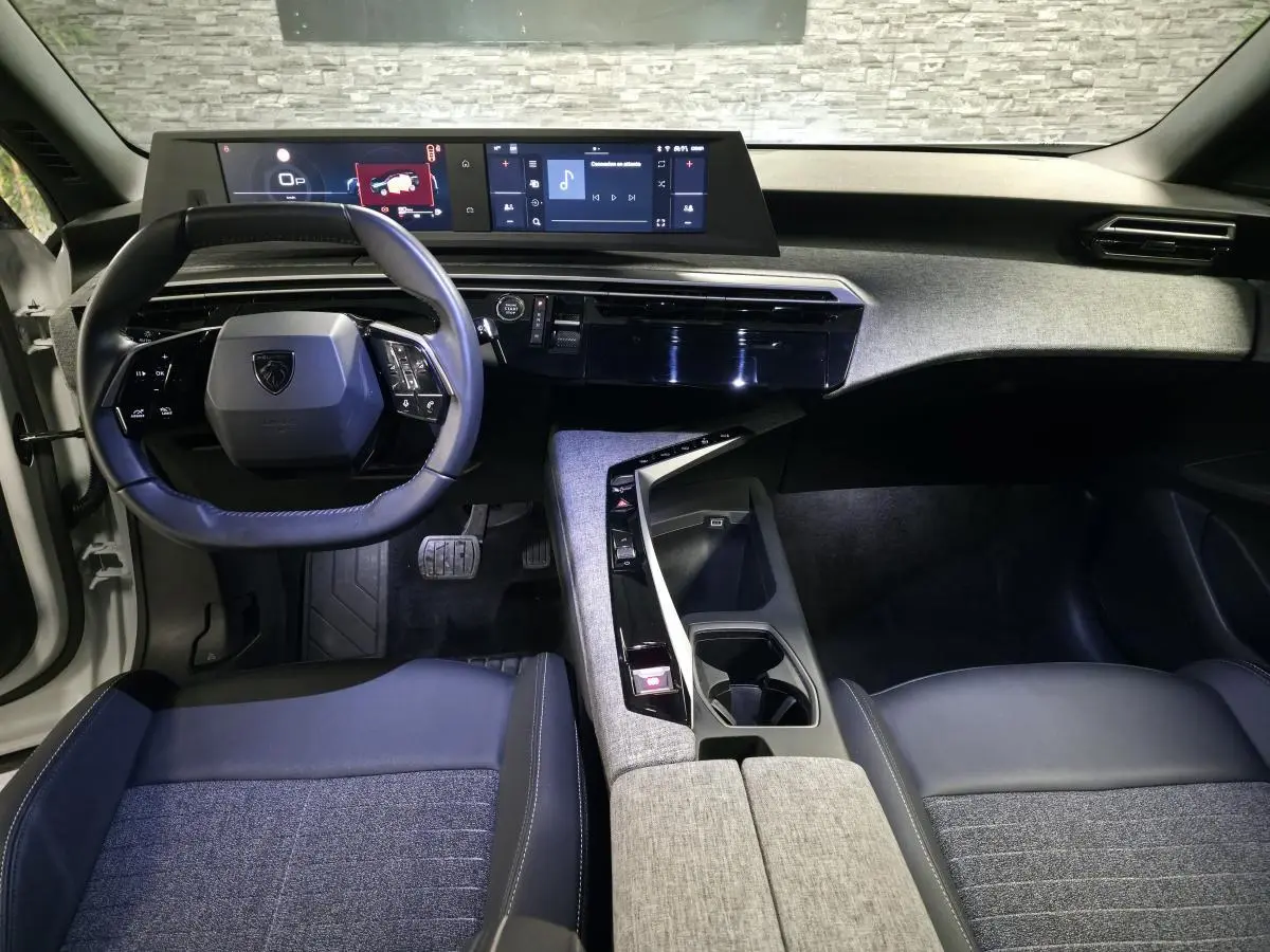 Vue intérieure avant du Peugeot 5008 2025, tableau de bord noir avec double écran HD et volant compact cuir.