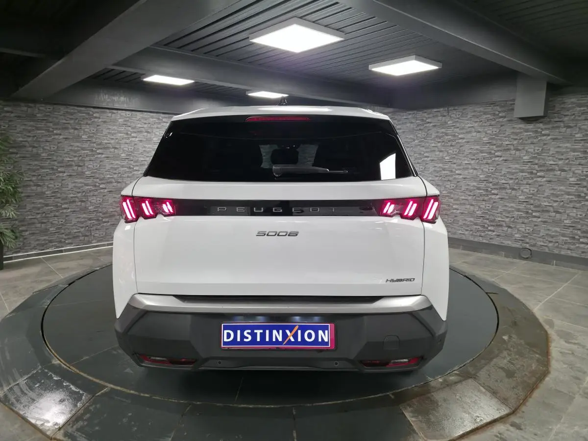 Vue arrière d'un Peugeot 5008 blanc hybride 2025 avec feux arrière LED à 3 griffes et bandeau noir laqué.