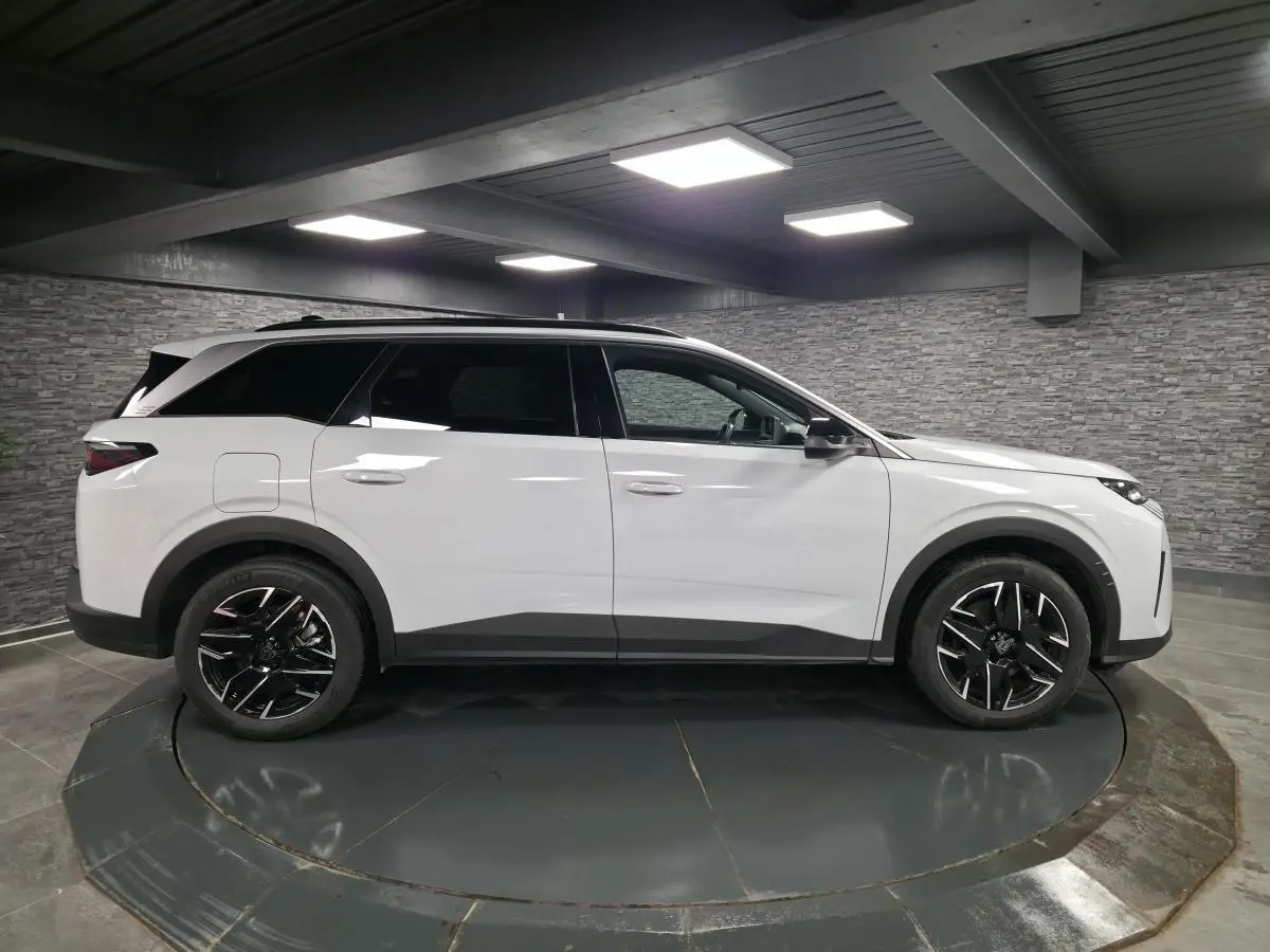 Vue latérale droite du Peugeot 5008 blanc 2025 avec jantes alliage noires et toit noir en intérieur showroom.