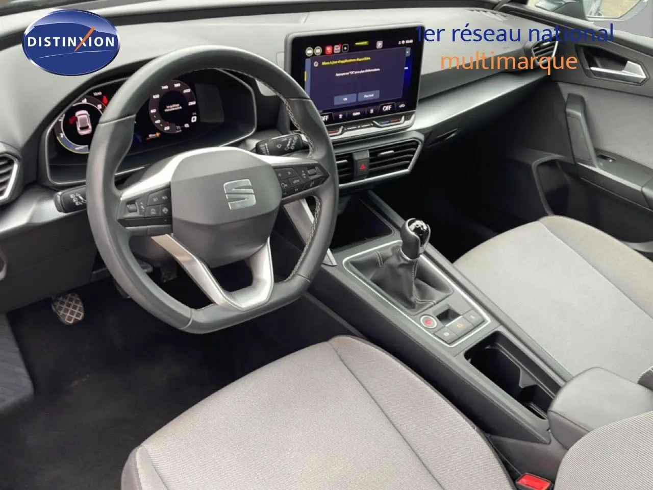 Vue intérieure centrée sur le poste de conduite du SEAT LEON 2025, volant cuir, tableau de bord digital et levier manuel.