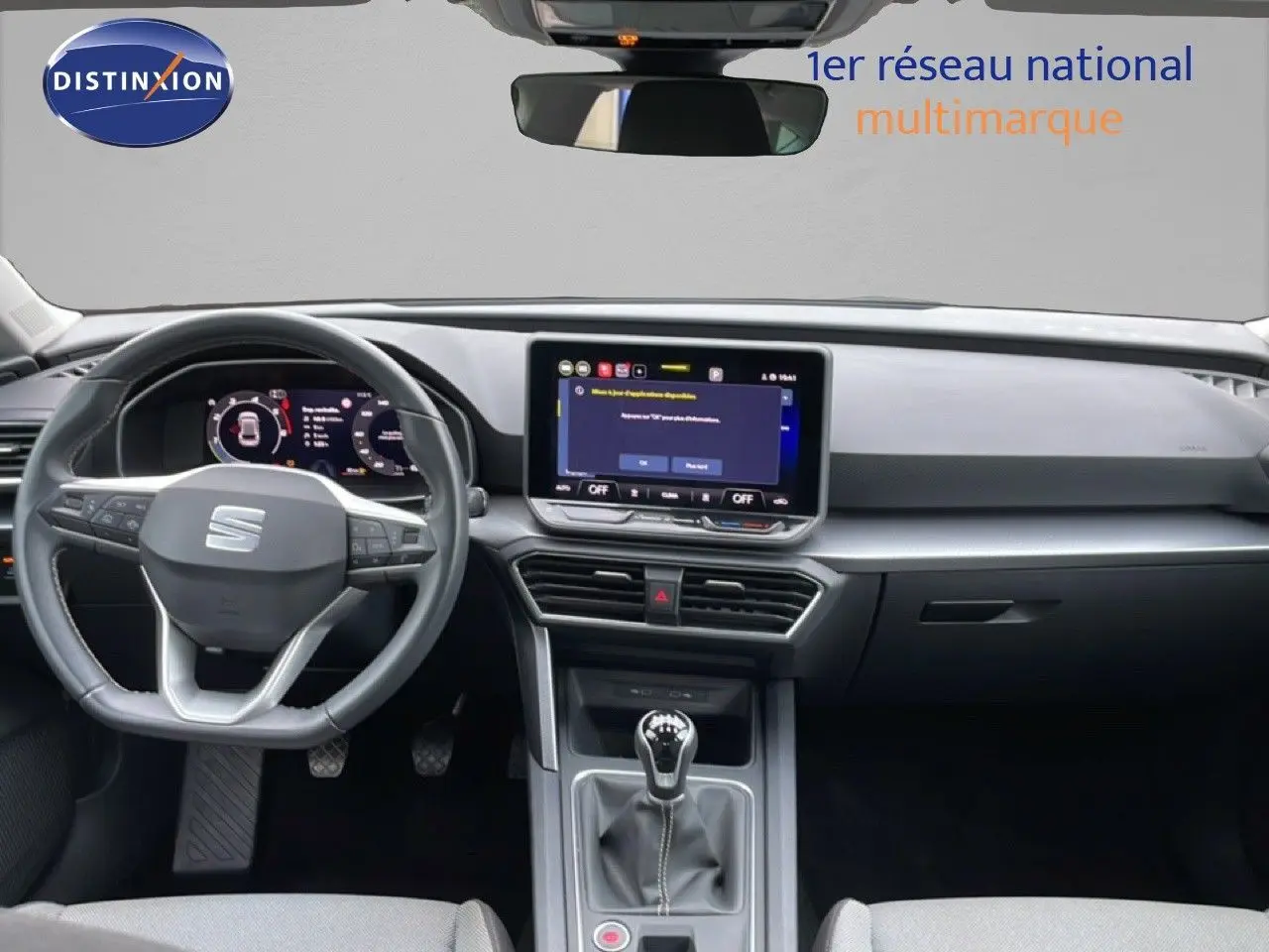 Vue intérieure frontale du poste de conduite du SEAT LEON gris magnétique, avec volant multifonction et écran tactile central.