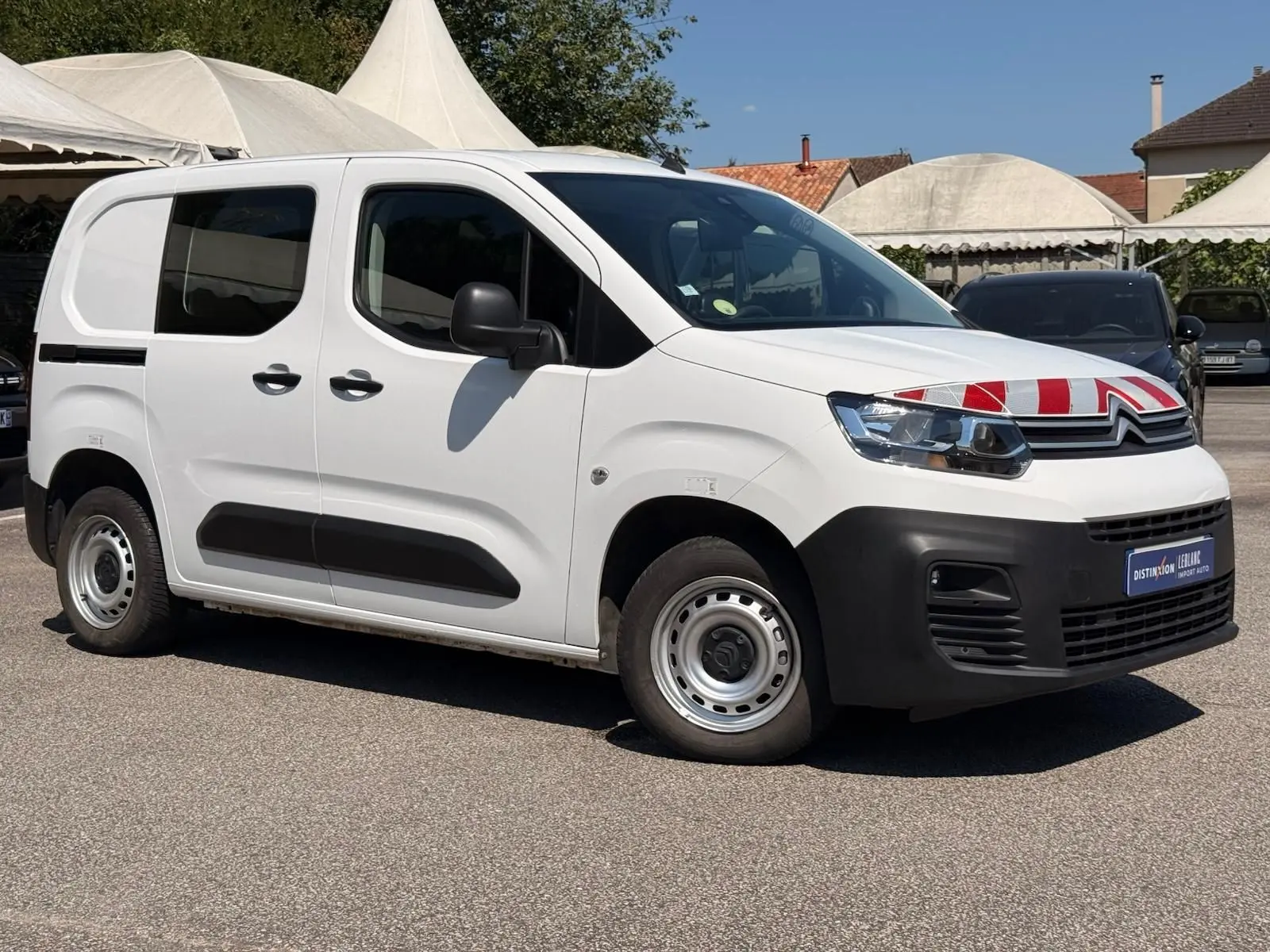 Vue 3/4 avant gauche d’un Citroën Berlingo Van blanc avec marquage rouge sur le capot et protections noires sur les bas de caisse.