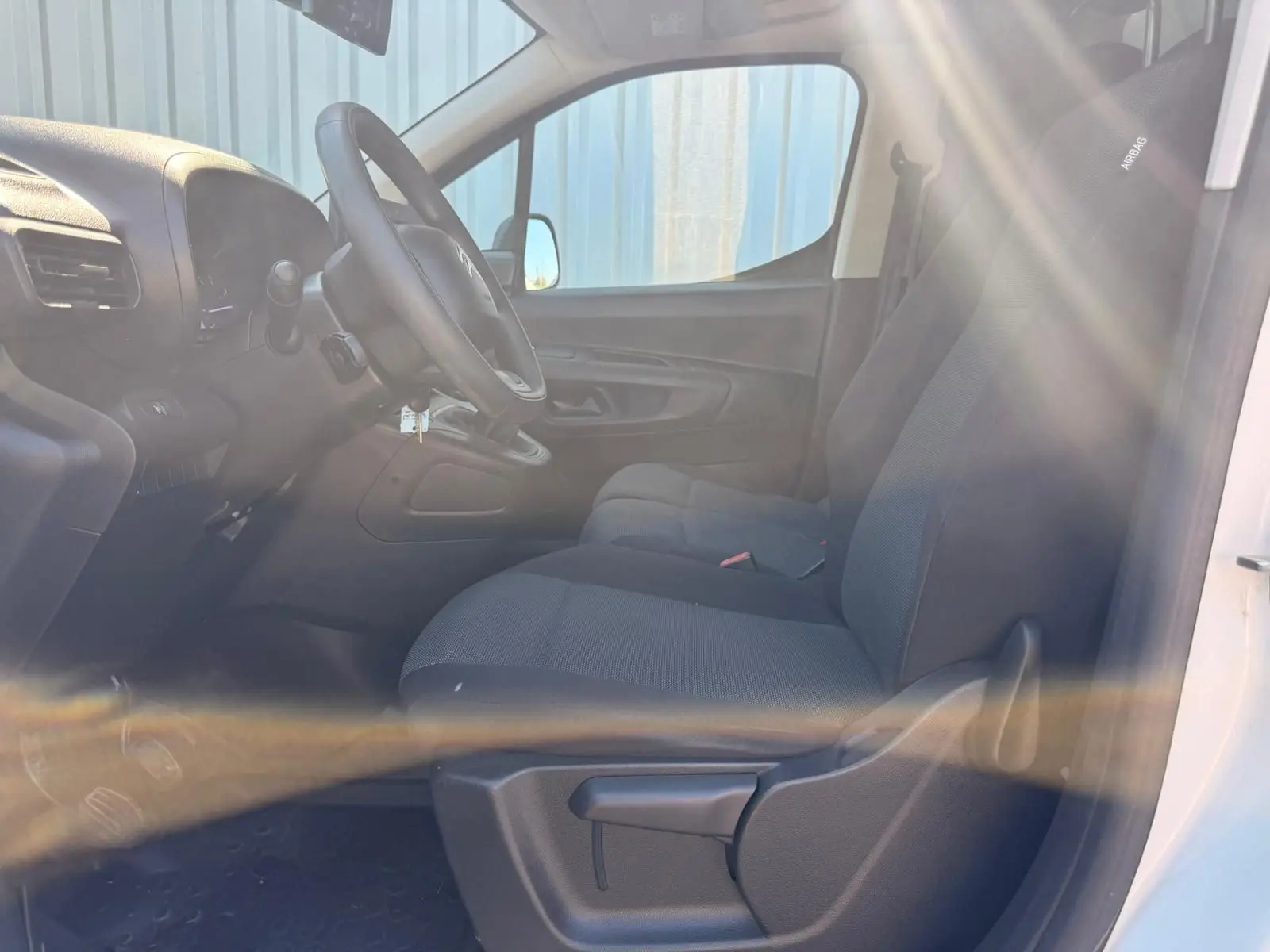 Vue intérieure côté conducteur du Citroën Berlingo blanc 2020, montrant les sièges en tissu et le tableau de bord.