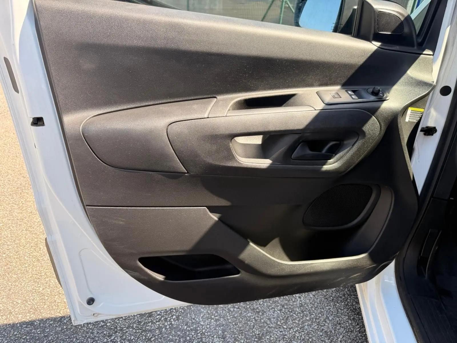 Vue intérieure de la porte avant gauche du Citroën Berlingo blanc, avec commandes de vitres et poignée noire.