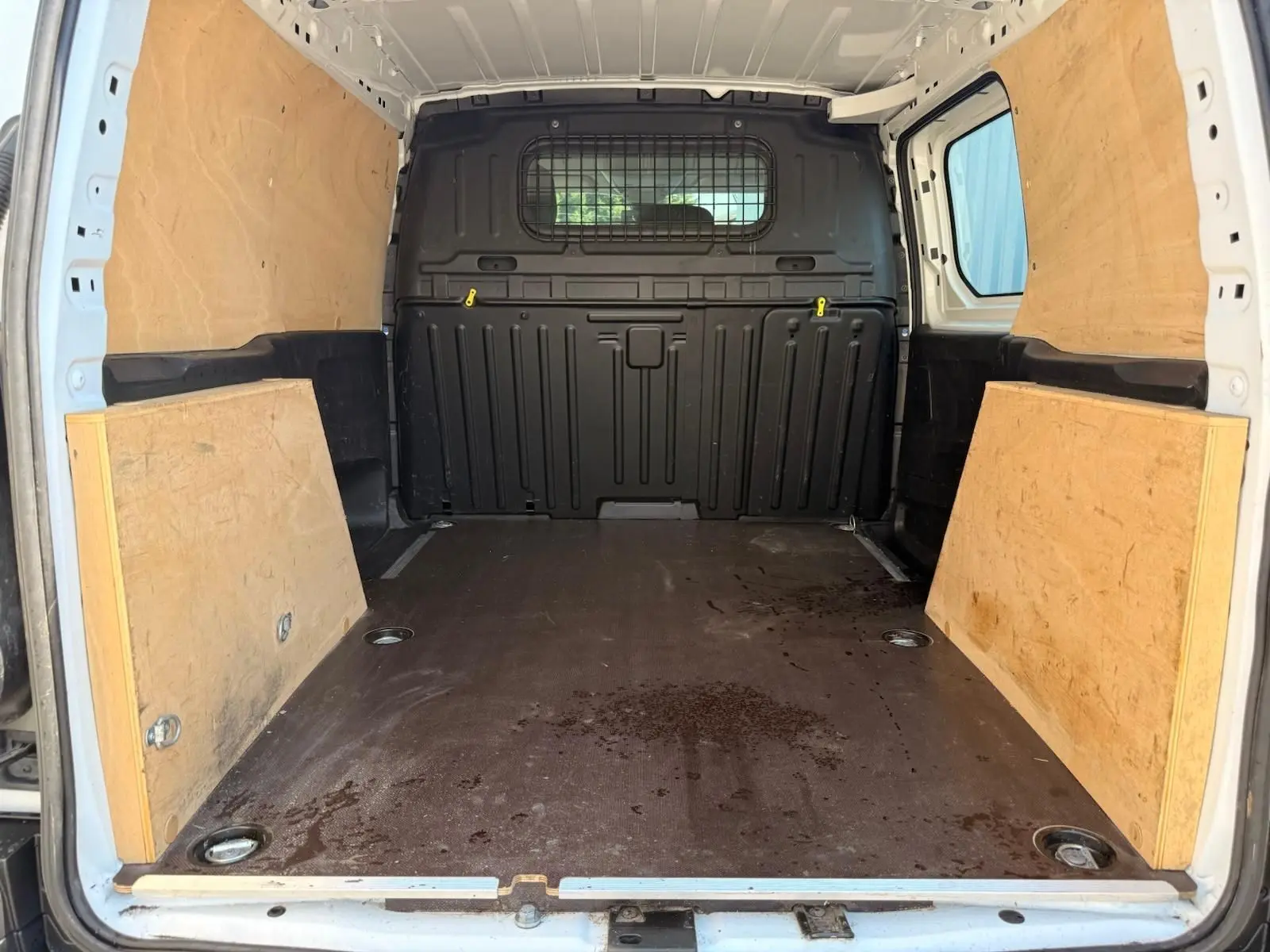 Intérieur du coffre du Citroën Berlingo Van blanc 2020, vue arrière ouverte avec parois en bois et cloison métallique noire.