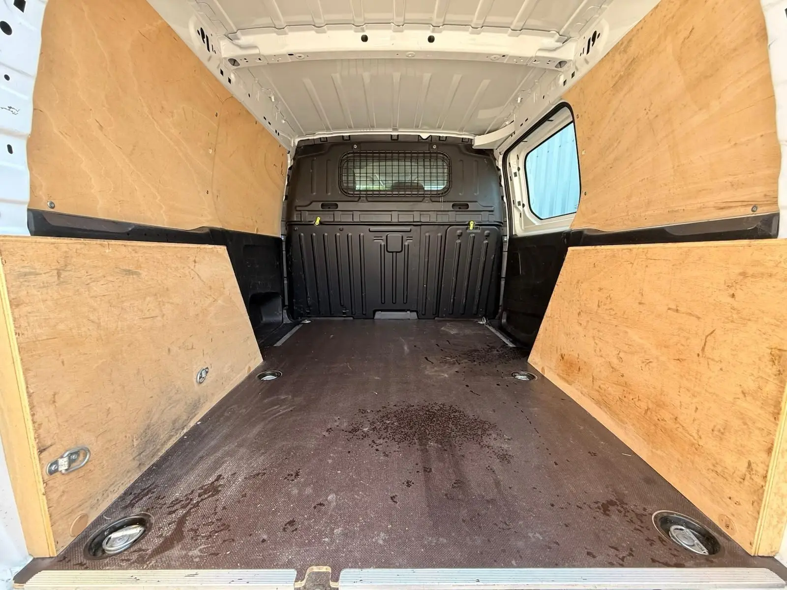 Intérieur du coffre du Citroën Berlingo Van blanc, vue de l'arrière montrant le plancher et les parois en bois.