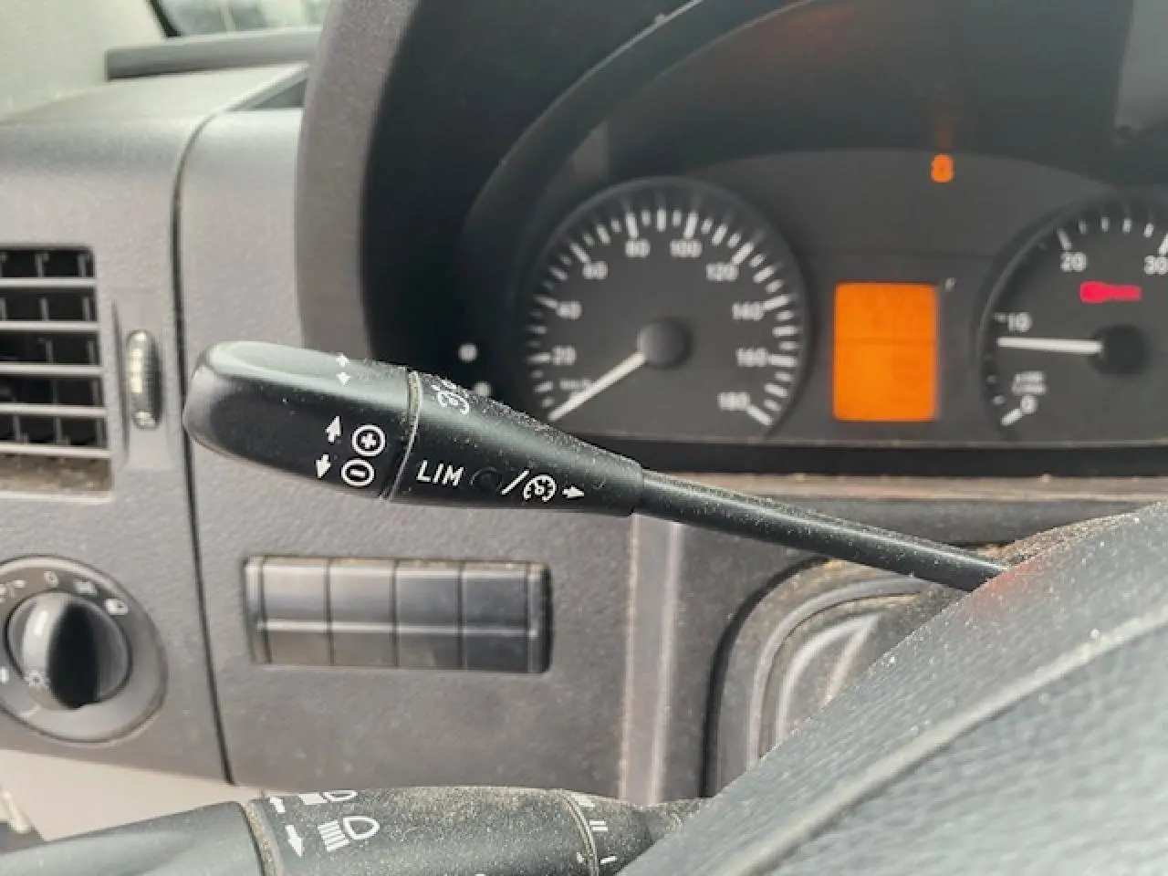 Gros plan sur la commande du régulateur et limiteur de vitesse dans le tableau de bord noir d'un Mercedes Sprinter blanc.