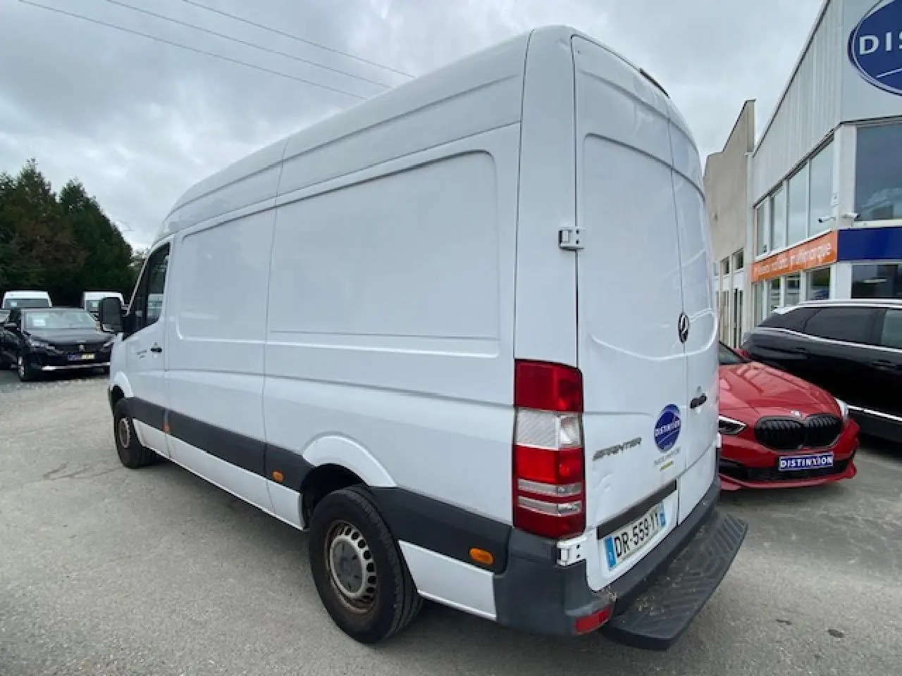 Vue 3/4 arrière droite d'un fourgon Mercedes Sprinter blanc de 2015 avec porte arrière fermée et feux rouges visibles.