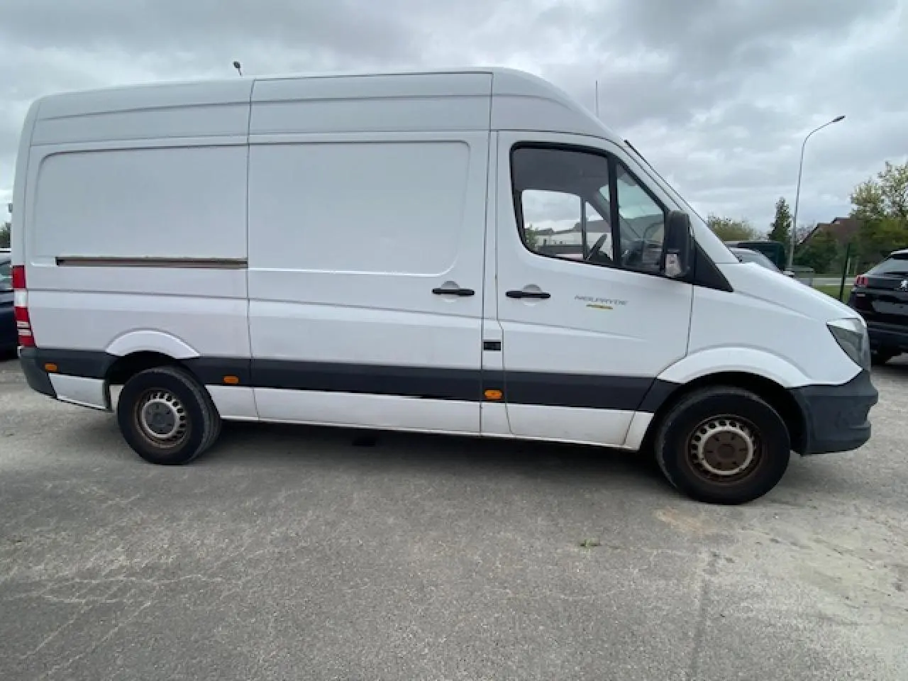 Profil côté gauche d'un fourgon Mercedes Sprinter blanc 2015 avec bande noire et feux latéraux orange visibles.