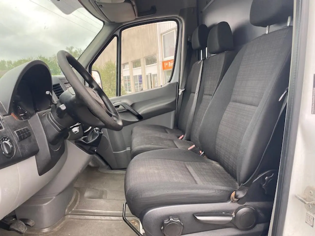 Vue intérieure côté conducteur du Mercedes Sprinter Fourgon blanc de 2015, montrant les sièges avant et le volant noir.