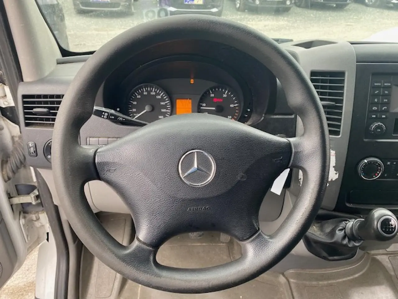 Vue intérieure centrée sur le volant noir Mercedes d'un Sprinter Fourgon blanc avec tableau de bord et levier manuel.