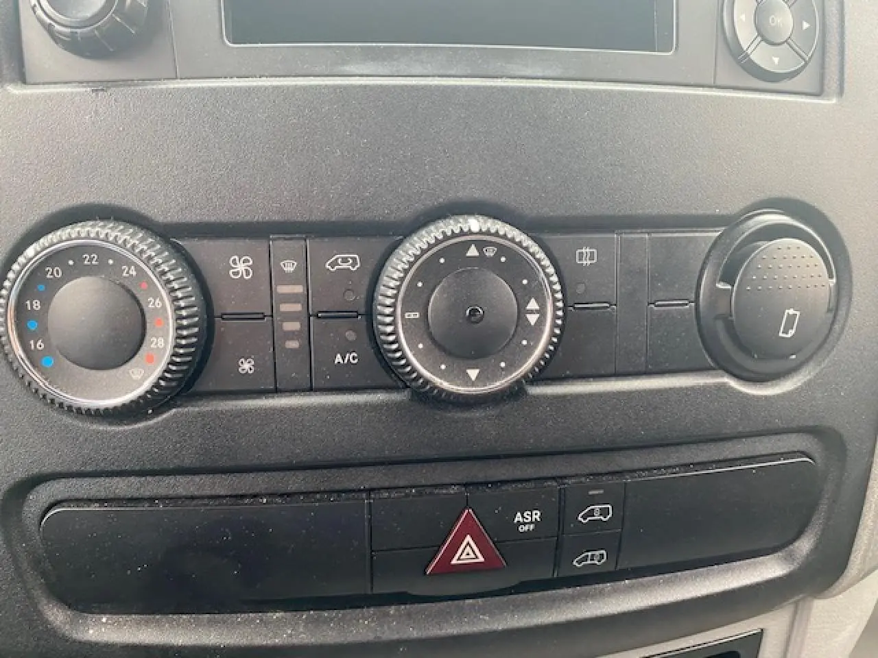 Gros plan sur les commandes de climatisation et les boutons de sécurité du tableau de bord du Mercedes Sprinter blanc.