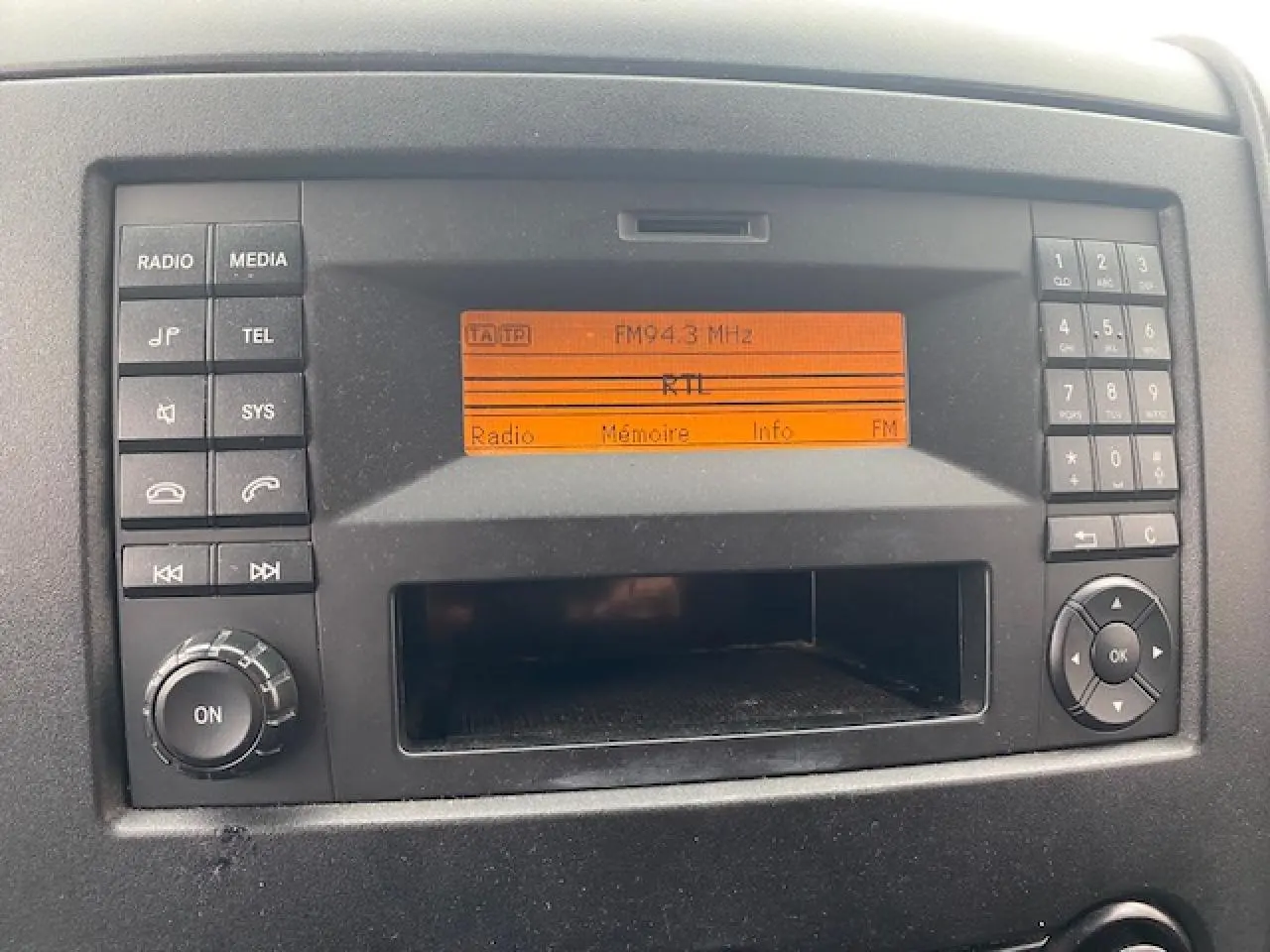 Gros plan sur la radio orange allumée du tableau de bord d'un Mercedes Sprinter Fourgon blanc de 2015.