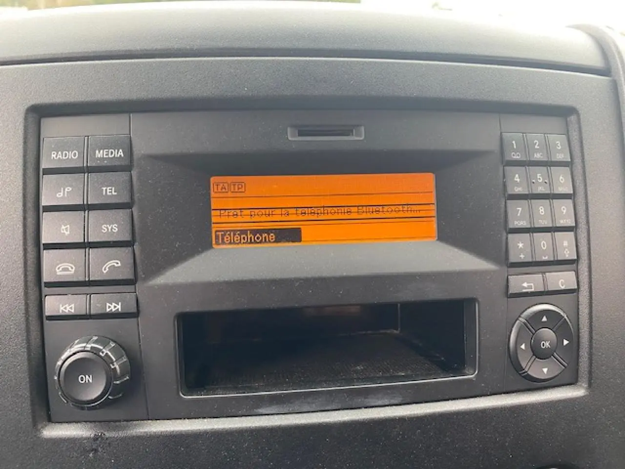 Console centrale du Mercedes Sprinter Fourgon 2015 avec écran orange affichant la fonction téléphone Bluetooth.