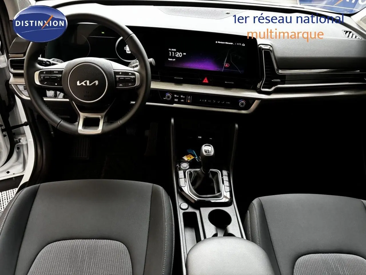 Vue intérieure frontale du tableau de bord et volant noir du Kia Sportage blanc nacré 2025 avec boîte manuelle.