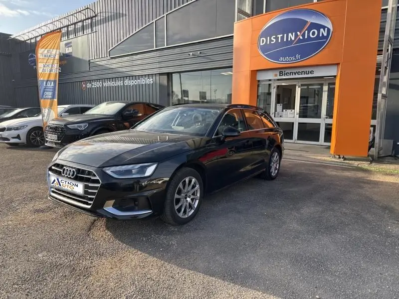 Audi A4 Avant noir brillant vue 3/4 avant droit, stationnée devant un garage avec enseigne orange Distinxion.
