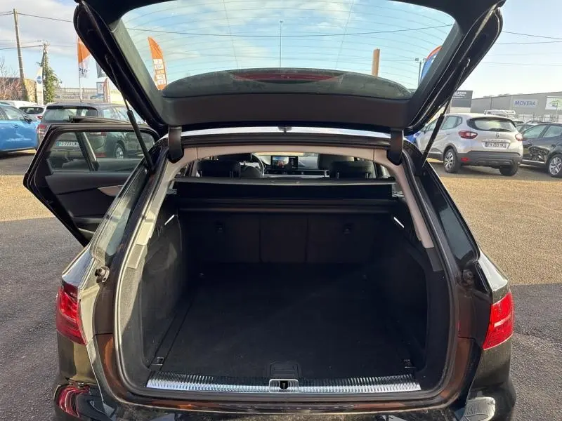 Vue arrière ouverte sur le coffre spacieux d'une Audi A4 Avant noir brillant, avec porte arrière relevée et porte latérale gauche ouverte.