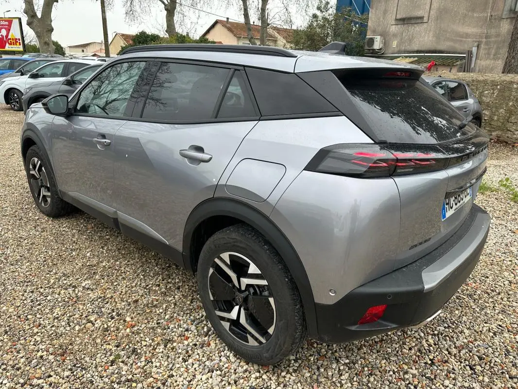 Vue 3/4 arrière droite d'un Peugeot 2008 Hybrid gris avec barres de toit et jantes alliage 17 pouces.