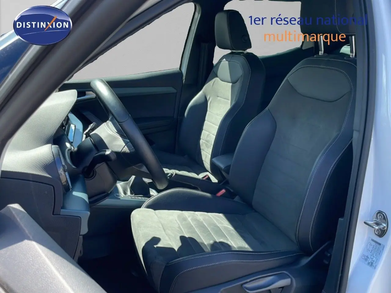 Vue intérieure côté conducteur du SEAT Arona 2025 blanc, montrant les sièges en cuir et alcantara noirs avec volant multifonction.